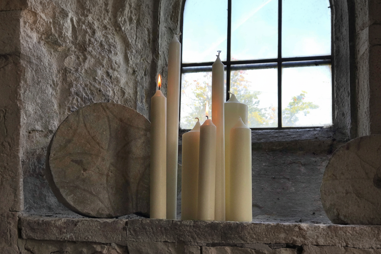 Ivory beeswax altar candles of varying heights arranged on a stone church altar, some lit with warm glowing flames