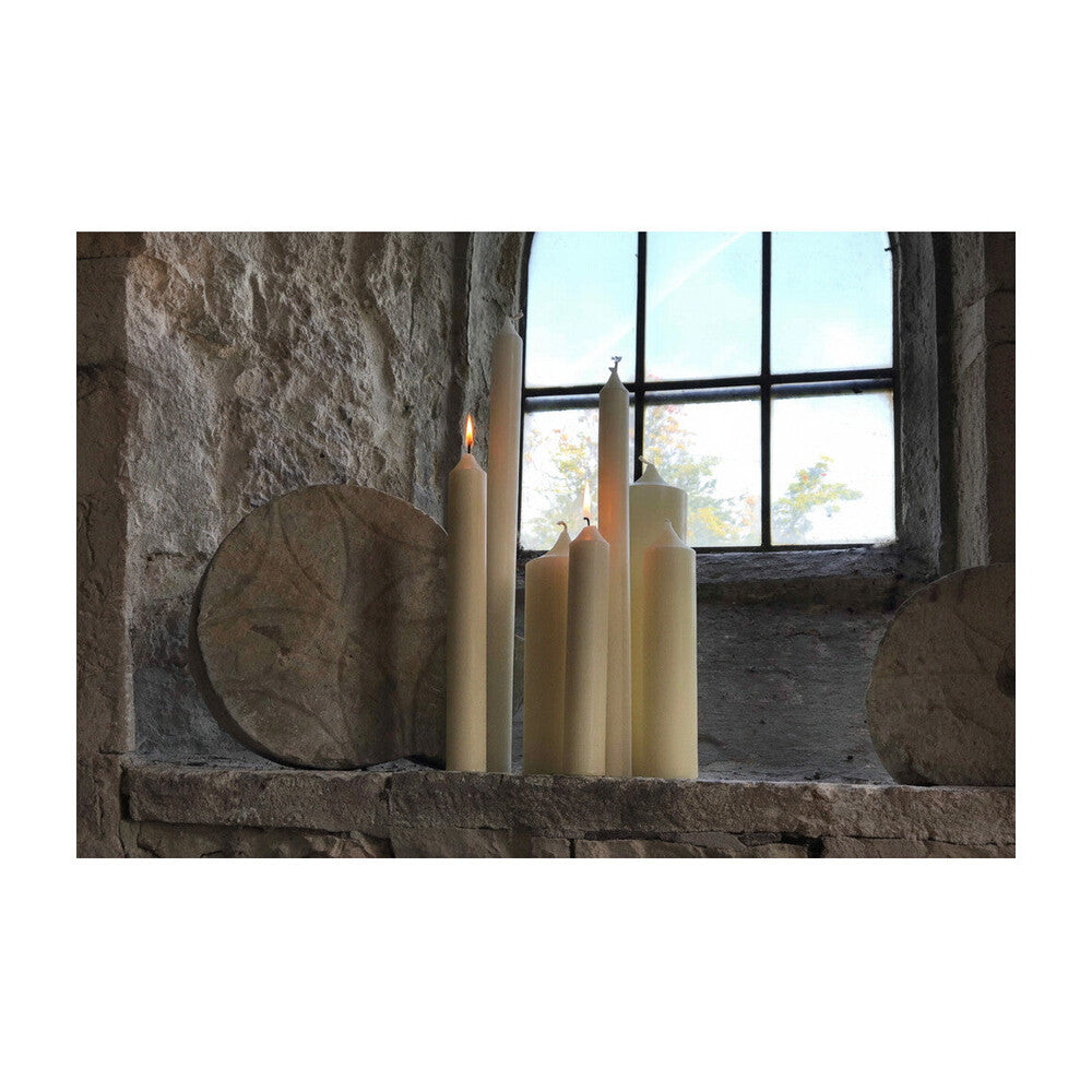 Ivory beeswax altar candles of varying heights arranged on a stone church altar, some lit with warm glowing flames